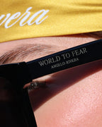 Person wearing black sunglasses with 'World to Fear' text, gold headband with 'Rivera' text.