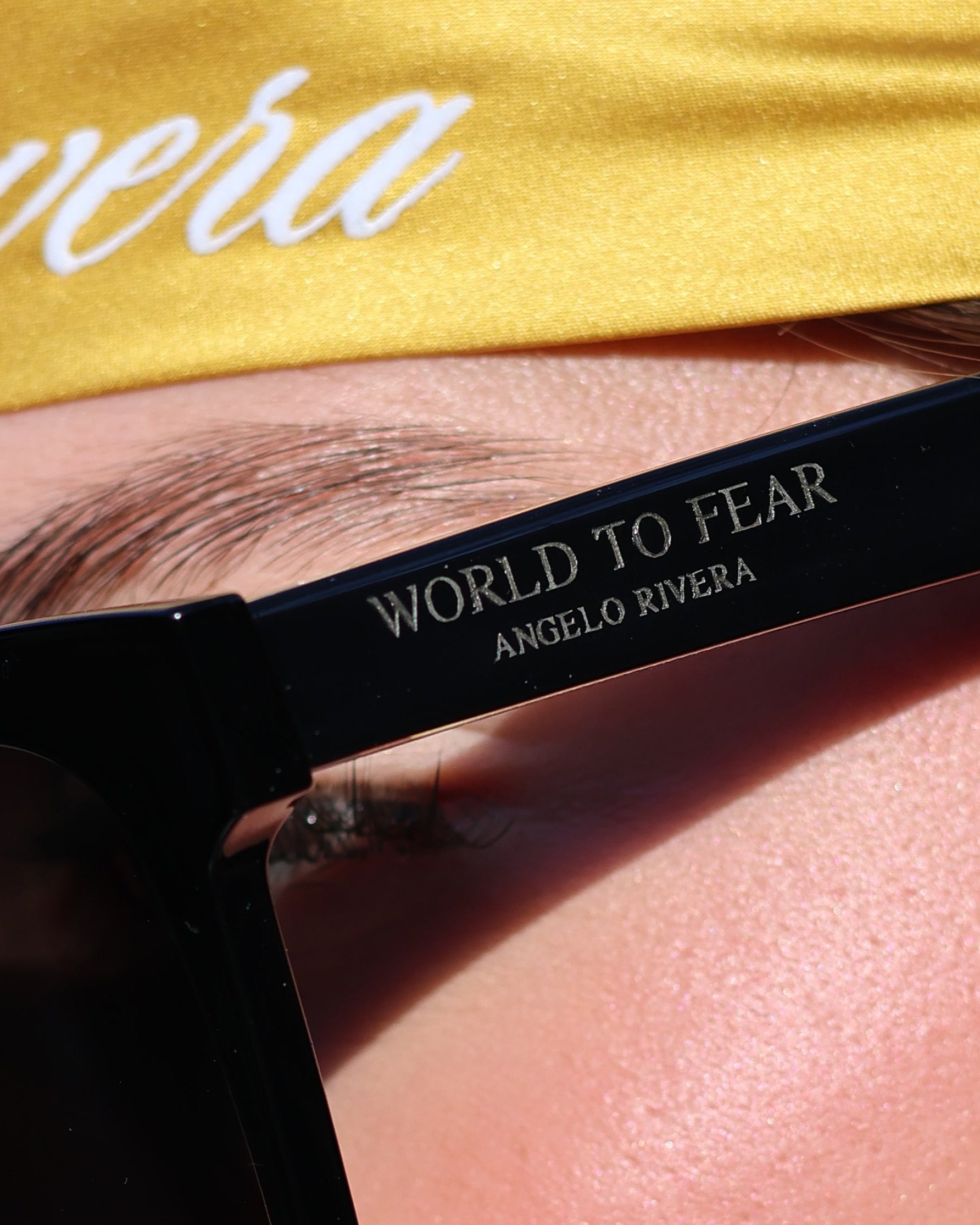 Person wearing black sunglasses with 'World to Fear' text, gold headband with 'Rivera' text.